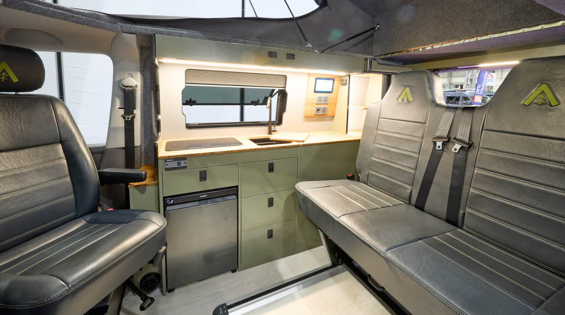Wildtracks Campervans Explorer has a cream floor with black leather upholstery.  The cabinets are green.  The rising roof is open.