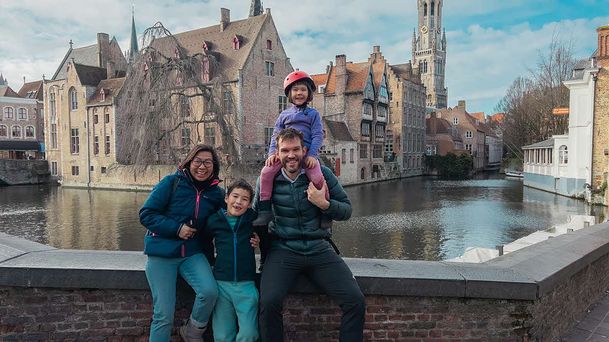 A photo of Marcus Leech and his family sitting on a wall with medieval Bruges in the background, for his blog, The Big European Odyssey