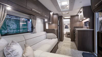 Buccaneer Bermuda interior, it is cream with dark wood furniture.  There is a L shaped sofa at the front.  The fixed bed is beyond the kitchen and there are large skylights.  
