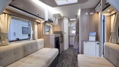 Interior of the Swift Sprite Alpine 4 DB with cream sofas, wood accents and a wooden floor.  The large roof light will let natural light flood in.  The rear washroom door is open.