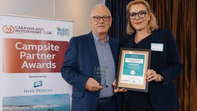 A Caravan and Motorhome Overseas Campsites Award Winner with the Chairman next to a sign showing Campsite Partner Awards, with Irish Ferries below it
