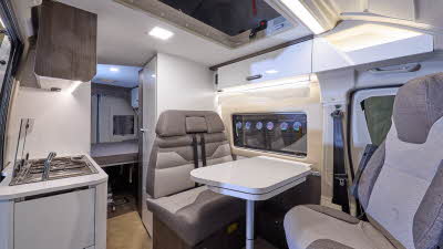 The Benimar Benivan 144 has wooden floor, with white cabinets.  The upholstery is two tone light and dark brown.  There is a fixed rear bed.  The pop top roof is open.  