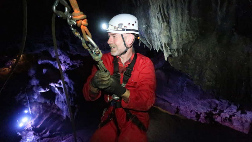 Man exploring cave wearing harness and safety gear