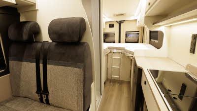 The Ace Motorhomes 1200 SLT has brown and cream upholstery with cream cabinets.  The hob and sink are in the front right and to the rear there is a fixed bed with a ladder for access.