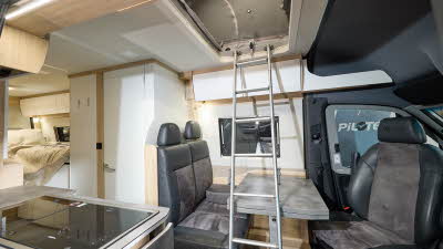 Frankia Yucon K-Peak’s interior has dark grey leather and suede upholstery.  The furniture is white with wooden surrounds.  There is a silver ladder leading to the roof.  There is a fixed bed at the rear and the hob is to the left.