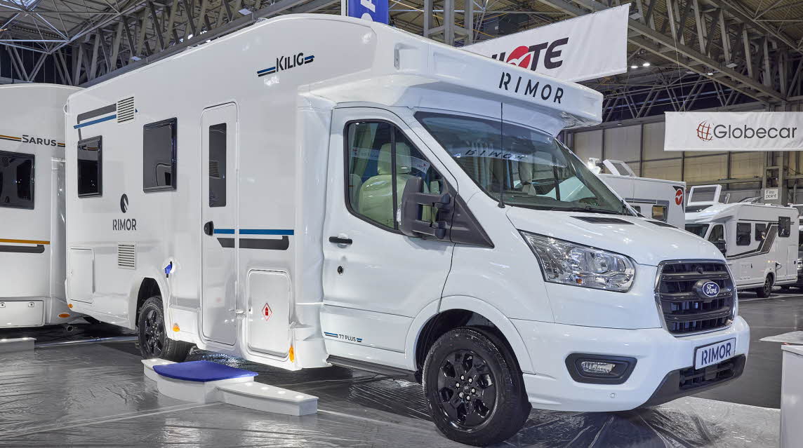 The Rimor Kilig 77 Plus is white with black and turquoise decals.  There are three white steps with a blue cover in front of the habitation door.