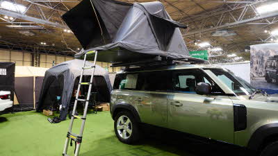 The Roof Space 4 is fully extended on a Land Rover Defender. The canvas is pale grey, with a black porch. There is a platform with a sturdy ladder to gain easy access.