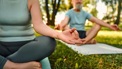 two figures sit cross legged on yoga mats surrounded by trees and grass