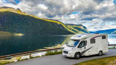 A motorhome driving next to a blue lake with green mountains rising above it