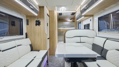 Roller Team Auto-Roller 707’s interior has white upholstery with black inserts.  Its furniture is pale wood.  At the rear there are fixed bunks.  The table is folded and can be extended.  The ceiling is textured fabric matching the upholstery.