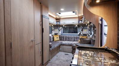Auto-Sleeper Broadway EL has grey embossed upholstery, with wooden furniture.  A hob with three gas rings and an induction hob is in the kitchen.  It has grey carpet.  There are patterned curtains in the windows.