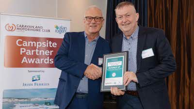 A Caravan and Motorhome Overseas Campsites Award Runner Up with the Chairman next to a sign showing Campsite Partner Awards, with Irish Ferries below it
