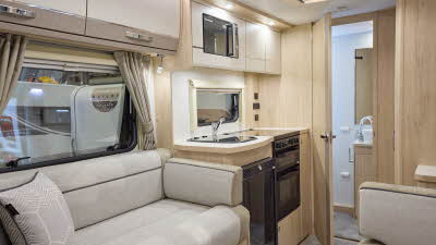 The Elddis Accordo 105 has a beige carpet, with cream and pale brown cabinets. The upholstery is cream and pale brown with dark brown piping. Through the opened interior door is a rear washroom.