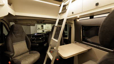 The Ace Motorhomes 1200 SLT has brown and cream upholstery with cream cabinets.  There is a ladder to gain access to the roof bed