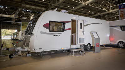 Elddis Avante 860 exterior is grey and white with black and red decals.  The door is open and there is a metal step to gain easy access to the interior.