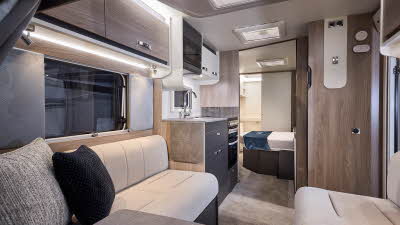 Interior of the Swift Challenger 580 with cream sofas, cosy cushions and beige carpets.  The three sky lights will let natural light flood in.  Beyond the fixed bed the door to the washroom is open.