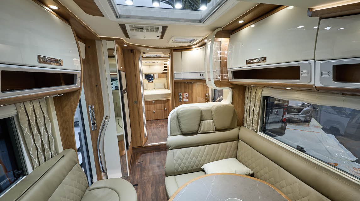 Carthago chic s-plus I 64 XL QB’s interior has beige leather upholstery.  The furniture is wooden with cream doors.  There is a large skylight.  There is a fixed bed to the rear.  