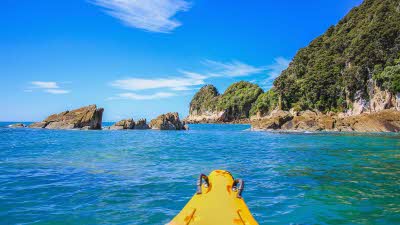 The front of a kayak looking out over the rocky cliffs and beautiful blue waters