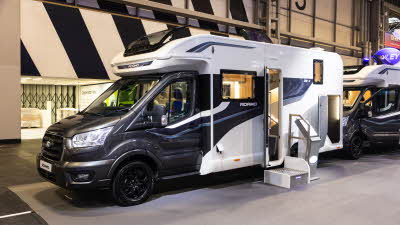 The Bailey Adamo 69-4 has a black cab and a white coachbuilt body, its sunroof and habitation door is open.  There is a step in front of the habitation door to gain easy access.  The garage door at the rear is also open.