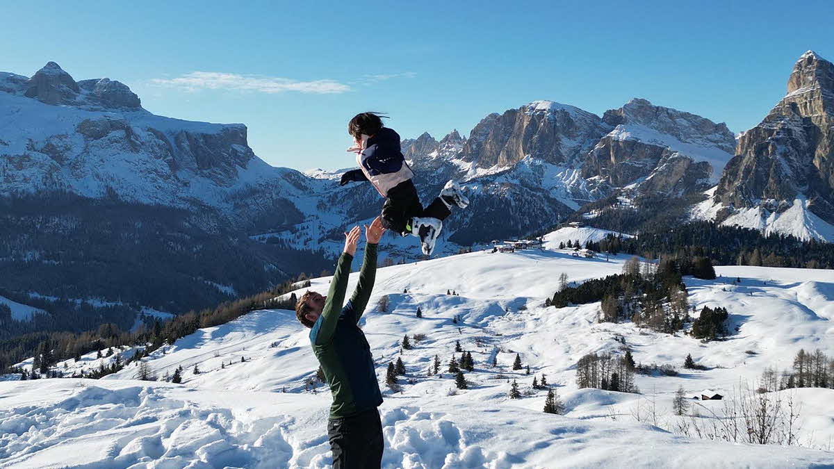 The blogger Marcus Leech throwing his child into the air on a snowy mountain in the Dolomites.