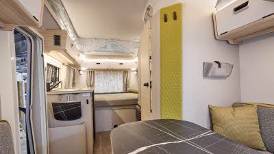 Interior of the Eriba Touring 530 Urban with grey sofas, lime green accents and a wooden floor.  To the rear there is a large fixed bed.