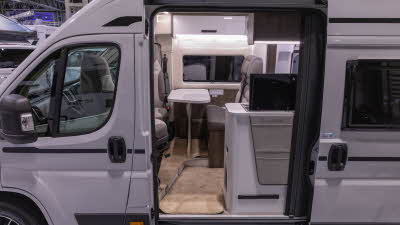 The Benimar Benivan 122 is white, its sliding door is open showing the swivelled front seats with a white table.
