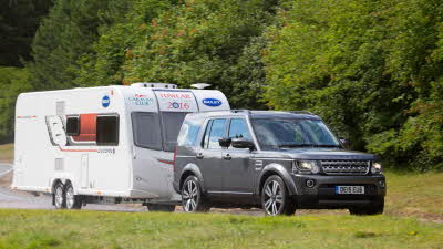 Grey Land Rover towing a caravan with trees in background