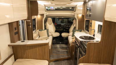 The Buccaneer Quantum F-4S has cream and fawn coloured upholstery.  It has matching cabinets with wood panels.  The front seats are swivelled to face into the van.