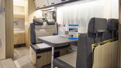 The Sun Living A Series 70DK has beige carpet and its upholstery is dark brown with cream inserts. The cabinets are white and dark wood. Towards the rear there are fixed bunks.