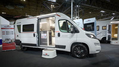 Roller Team Livingstone 6’s exterior is white.  It has grey and red decals.  The habitation door is open revealing the seating area and there is a large white step to gain easy access.
