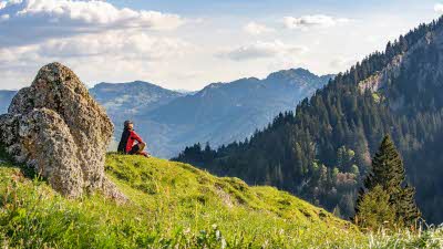 A hiker sitting looking over the tree covers mountains