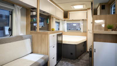 Knaus Sport 450 FU’s interior has wooden furniture with cream doors.  Its upholstery is cream with grey edging.  There is a fixed transverse bed to the rear.