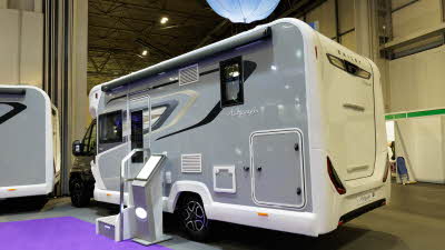 The Bailey Autograph 72-2 has a black cab and grey coachbuilt body.  It has black, cream and grey decals.  There is a step outside the habitation door with an interactive stand next to it.  Above it is a blue Bailey umbrella.