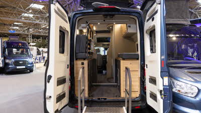 The Bailey Endeavour B65's rear is showing the rear bed in the lifted position.  The cabinets are made from pale wood.