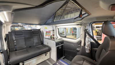 Adria Active Duo's interior has dark grey leather upholstery with white and black units.  The zipped door with access to the roof is partially opened.  The front passenger’s seat is swivelled.