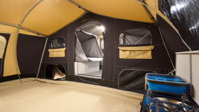 The Raclet Safari GL has a dark cream coloured canvas.  The bedroom and windows doors are open revealing the interior.  There is a matching groundsheet on the floor, upon which is the kitchen unit.  