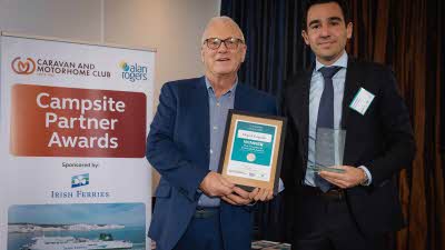 A Caravan and Motorhome Overseas Campsites Award Winner with the Chairman next to a sign showing Campsite Partner Awards, with Irish Ferries below it
