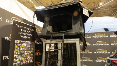 The RoofBunk Adventurer has black canvas.  Its door is open.  There is a black ladder to gain access.