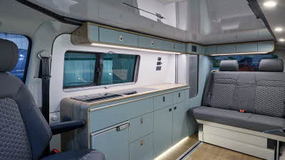 Ecowagon Expo+’s interior has dark grey upholstery.  The furniture is wooden with duck egg blue doors.  The two rear seats have seat belts.  The rising roof is down and the access panel is grey.