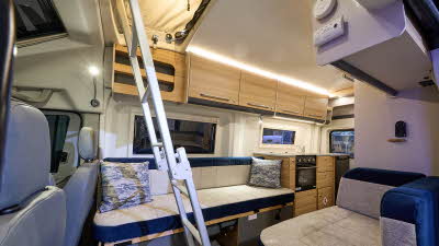 Bailey Endeavour B64’s interior has beige and dark blue fabric upholstery with blue/white cushions.  The furniture is wooden.  There is a silver ladder to gain access to the bed in the rising roof.  The kitchen is to the rear.