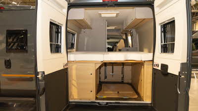 The Elddis Whirlwind GTV 563 has a rear fixed bed.  The top lockers are cream with a wooden panel underneath.  Beneath the fixed bed is a storage area with further wooden cabinets.