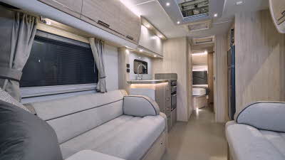 Elddis Crusader Tempest’s interior has grey upholstery with dark grey accents.  It has pale wooden furniture.  The kitchen is in the middle and the bedroom door is open revealing a fixed French transverse bed.