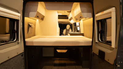 The VANTourer 600 D has brown and cream upholstery with matching cabinets.  The rear doors are open revealing the rear fixed double bed.