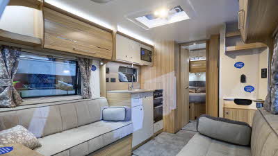 Bailey Pegasus Grande GT75 Amalfi’s interior has wooden furniture with grey upholstery.  The kitchen is in the middle with a bedroom with a fixed island double bed the rear.  There is a roof light above the kitchen.