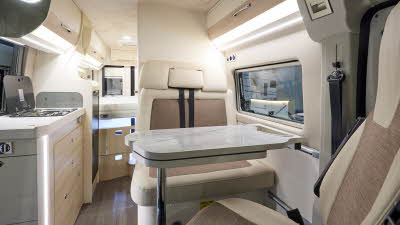 Eura Mobil Van 635 has wooden flooring with mid brown and cream upholstery.  The cabinets are cream and pale wood.  There is a step to reach the fixed rear bed.