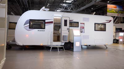 Elddis Avanté 840's exterior is white with a grey and dark red patterned decal from the front to the rear.  The entrance door is open and there is a large metal step to gain easy access.  There is an interactive stand to the right.