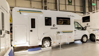 The Rimor Kilig 79 has a white exterior with green and gold decals.  There is a large step outside the habitation door.  There is an information stand next to the van.