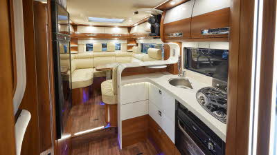 Carthago liner-for-two I 53 Fiat has leather upholstery with curved cream overhead lockers with wooden surrounds.  There is a large oval table.  There is a wooden floor, with a step to the kitchen, beyond this there is a fixed rear bed.