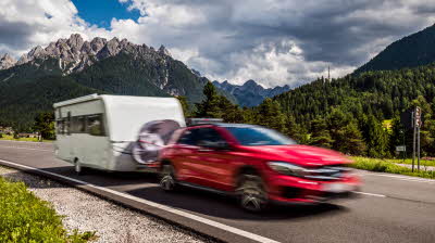 red car towing a caravan through mountains