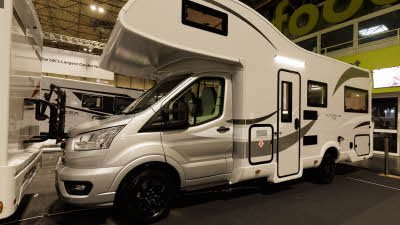 The Roller Team Auto-Roller 746 has a silver cab and white coachbuilt body.  It has black trims around the doors with bronze decals.  